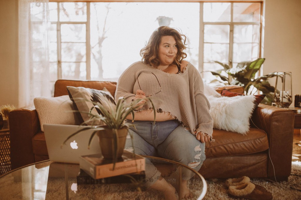 Corissa is sitting on a couch smiling off to the side.