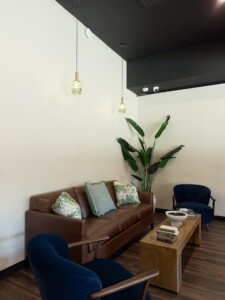 A brown couch and two deep blue armchairs surround a coffee table with decorative books and more decor