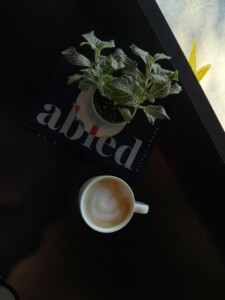 A plant and mug with latte art rest on a table with the word art 'abled'
